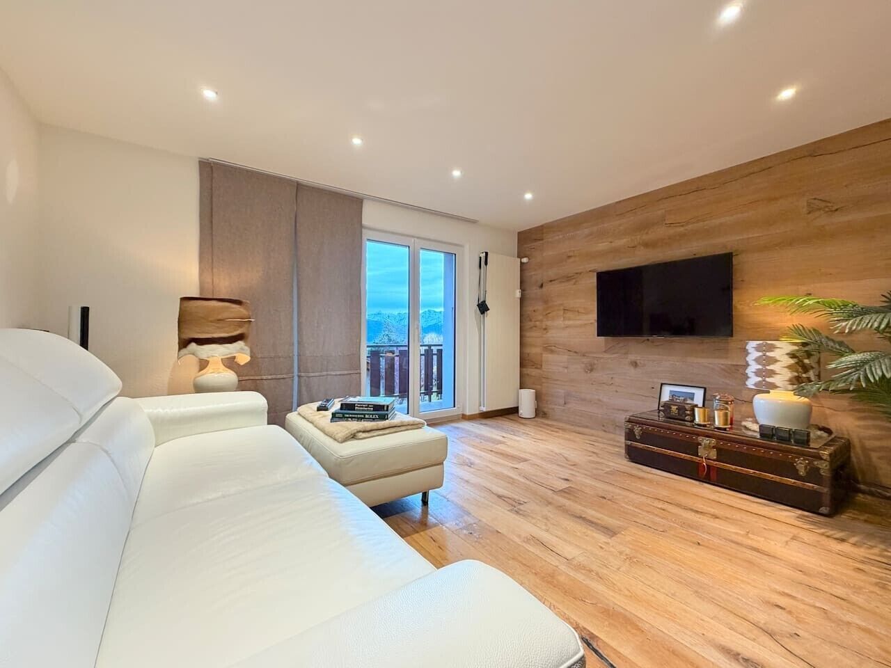 Una sala de estar moderna con un sofá, una mesita baja con libros, un mueble de madera y un televisor montado en la pared.