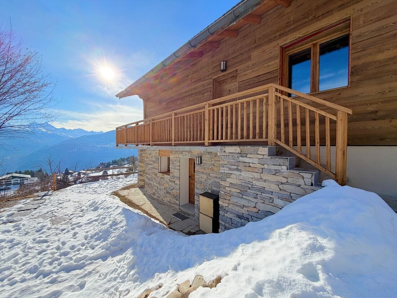 Une cabane en bois avec des fondations en pierre, un escalier en bois et une vue sur les montagnes en arrière-plan.