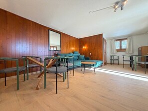 A spacious room with a wooden floor, a sofa, a dining table, and chairs. - A fully equipped chalet with a magnificent view of the Alps! (Crans-Montana)