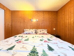 A bedroom with wooden panel walls, a bed with a festive bedspread, and a wall-mounted light fixture. - A fully equipped chalet with a magnificent view of the Alps! (Crans-Montana)