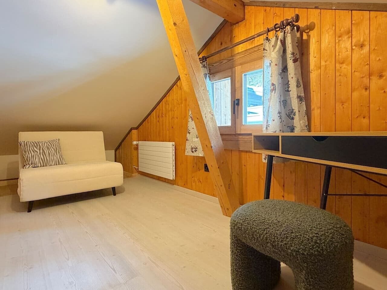 A loft-style room with a sloped ceiling, a white sofa, a small stool, and a wooden ceiling beam.