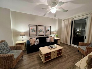 A living room with a black sofa, two side tables with lamps, a ceiling fan, and a sliding glass door. - #425 Fontainebleau Updated Beachfront Condo (Panama City Beach)