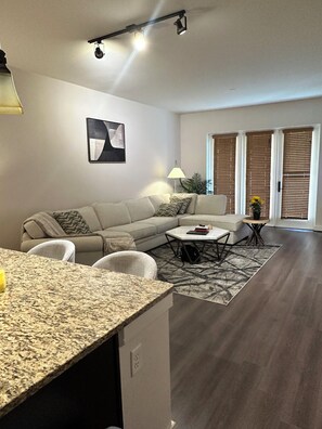 A modern living room with a sectional sofa, a dining table, and a kitchen area with granite countertops. - Cozy 1-bedroom apartment with backyard in Postoak/ Galleria Houston (Houston)