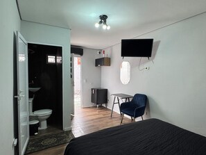 A compact room with a bed, a desk, a chair, a TV, and a bathroom with a toilet and sink.