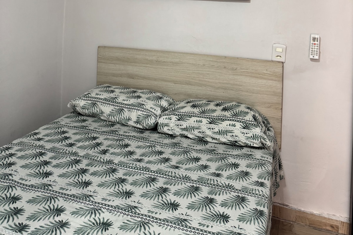 A bedroom with a bed, a wall-mounted painting, and a bedside table.