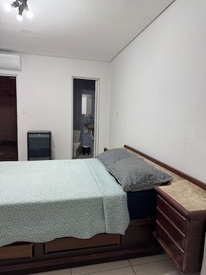 Un dormitorio con cama, cómoda, televisión y baño visible a través de una puerta abierta.