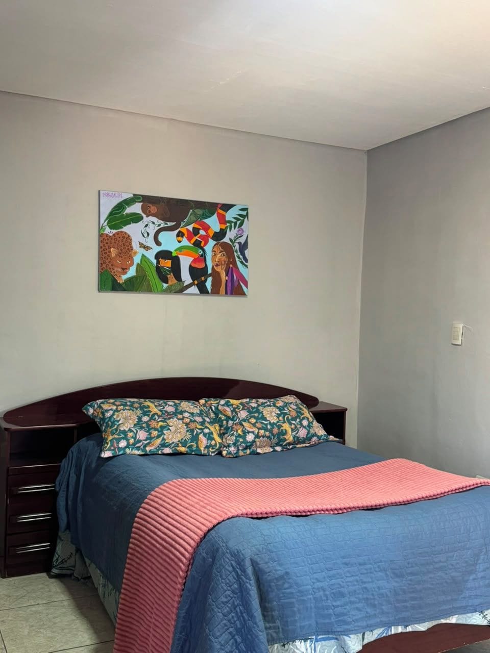 Een slaapkamer met een bed, een aan de muur hangend schilderij en een nachtkastje.