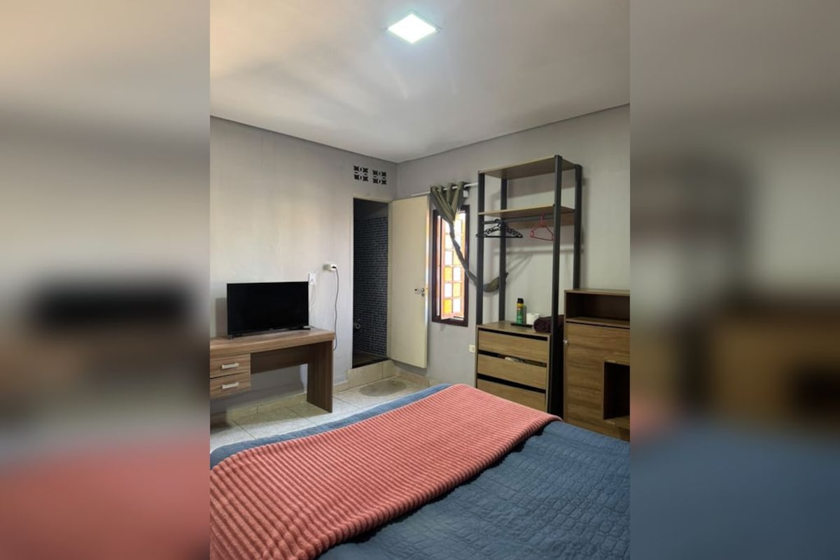 A bedroom with a bed, a desk, a TV, a wardrobe, and a mirror.