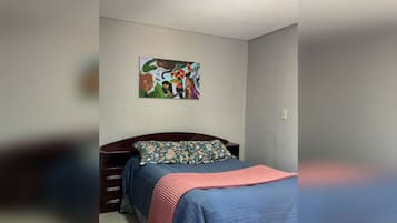 A bedroom with a bed, a nightstand, a dresser, and a painting on the wall.