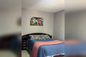 A bedroom with a bed, a nightstand, a dresser, and a painting on the wall.