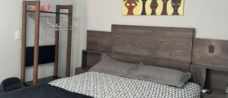 A bedroom with a bed, a bedside table, a wardrobe, and a wall-mounted artwork.