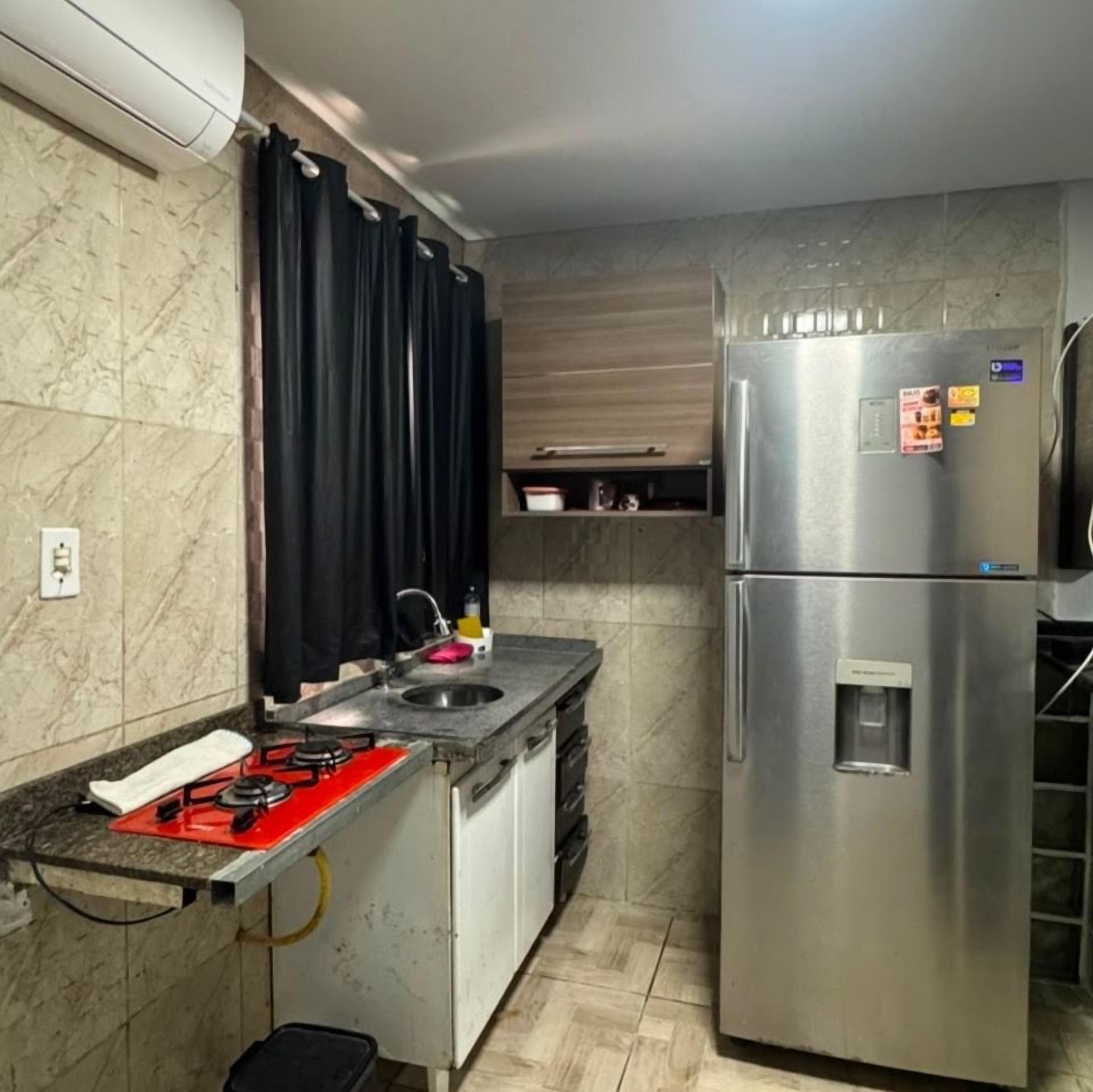 Una cocina con un refrigerador de acero inoxidable, una estufa a gas, un lavamanos y una cortina negra.