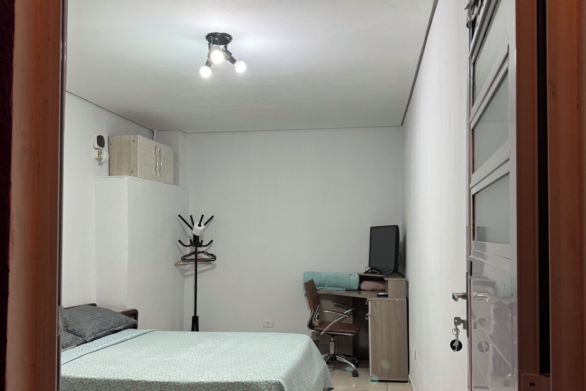 A bedroom with a bed, a desk, a chair, a wardrobe, and a ceiling light fixture.