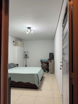 Un dormitorio con cama, escritorio, silla, armario y lámpara en el techo.