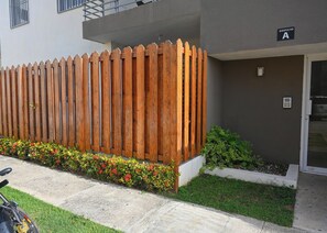 Ein Gebäude mit Holzzaun, ein kleiner Garten mit roten Blumen und ein Schild, das den Eingang zeigt.