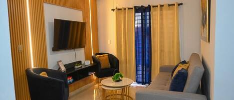 Una sala de estar moderna con un televisor de pantalla plana, dos sillones, un sofá, una mesa de centro y un ventilador de techo.