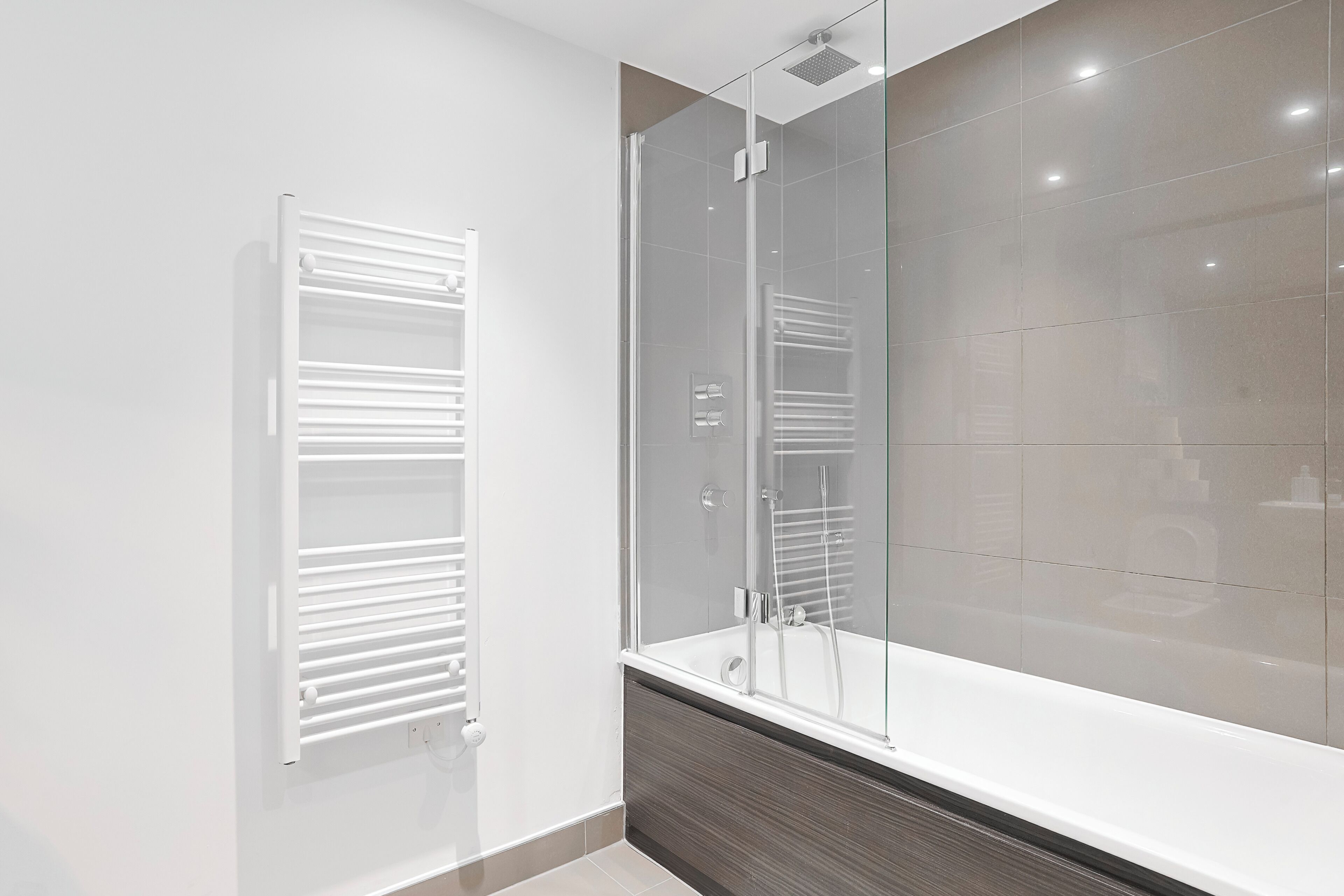 A modern bathroom with a glass shower enclosure, a white bathtub, and a towel rack.