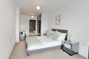 Une chambre à coucher moderne, comprenant un lit, des tables de chevet, une commode, un miroir et une porte donnant sur une salle de bain.