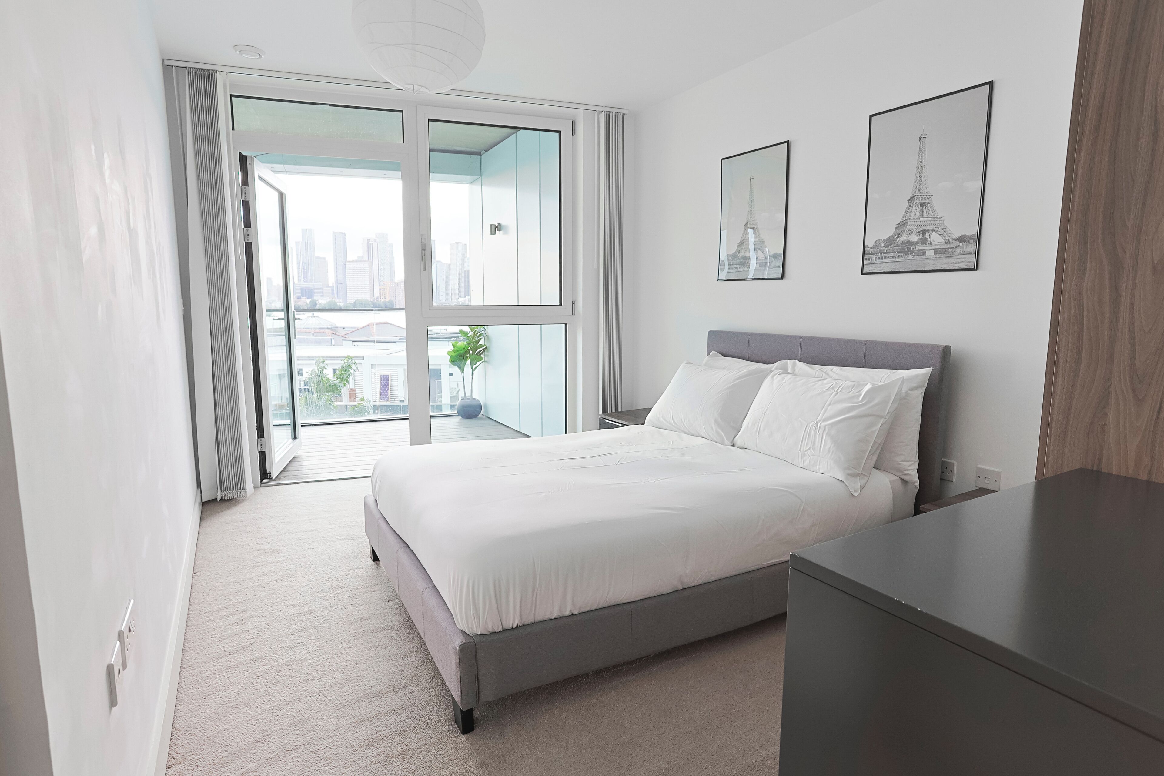 A modern bedroom with a large bed, a nightstand, a dresser, and two framed pictures of the Eiffel Tower.
