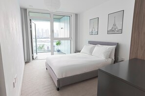 A modern bedroom with a large bed, a nightstand, a dresser, and two framed pictures of the Eiffel Tower. - Luxury 2-Bed Greenwich Apartment with River Views & Private Balcony (London)