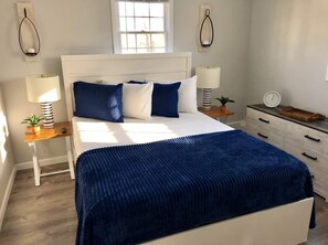 Un dormitorio con cama, mesitas de noche, lámpara, reloj y ventana.