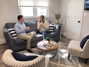 A living room with a grey sofa, striped armchairs, a coffee table with remote control, and a potted plant. - Unit 4 - 3 Houses to Beach -  2 BR Apartment (Seaside Heights)