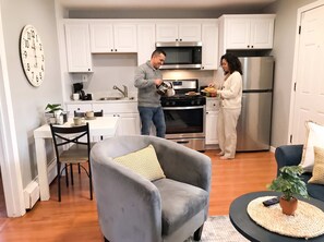 A modern kitchen with white cabinets, a stainless steel refrigerator, and a dining area with a grey armchair and a small table. - Unit 3 - Cozy 2 Bedroom Apartment Near Seaside Beach & Boardwalk (Seaside Heights)