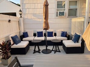 Eine Terrasse mit Gartenmöbeln, darunter Sofas und Tische, sowie ein Pergola mit Sonnenschirm.