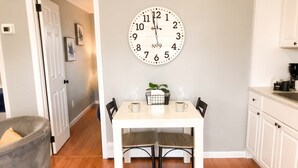 Un comedor con una mesa blanca, dos sillas, un reloj de pared y una cafetera.