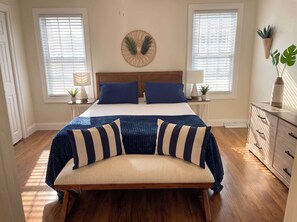 A bedroom with a bed, bedside tables, lamps, a bench, a dresser, and two windows with blinds. - Unit 1 - Ocean View - Third House from Beach & Boardwalk! - 2BR - Parking (Seaside Heights)