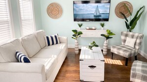 Ein Wohnzimmer mit Sofa, Sesseln, einem Couchtisch, einem Fernseher und Dekorationselementen.