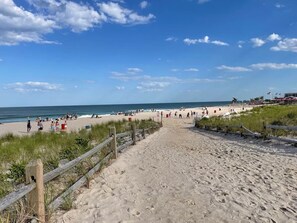Ein sandiger Strand mit einer Holzzaun, Menschen unterwegs und einem klaren Himmel.