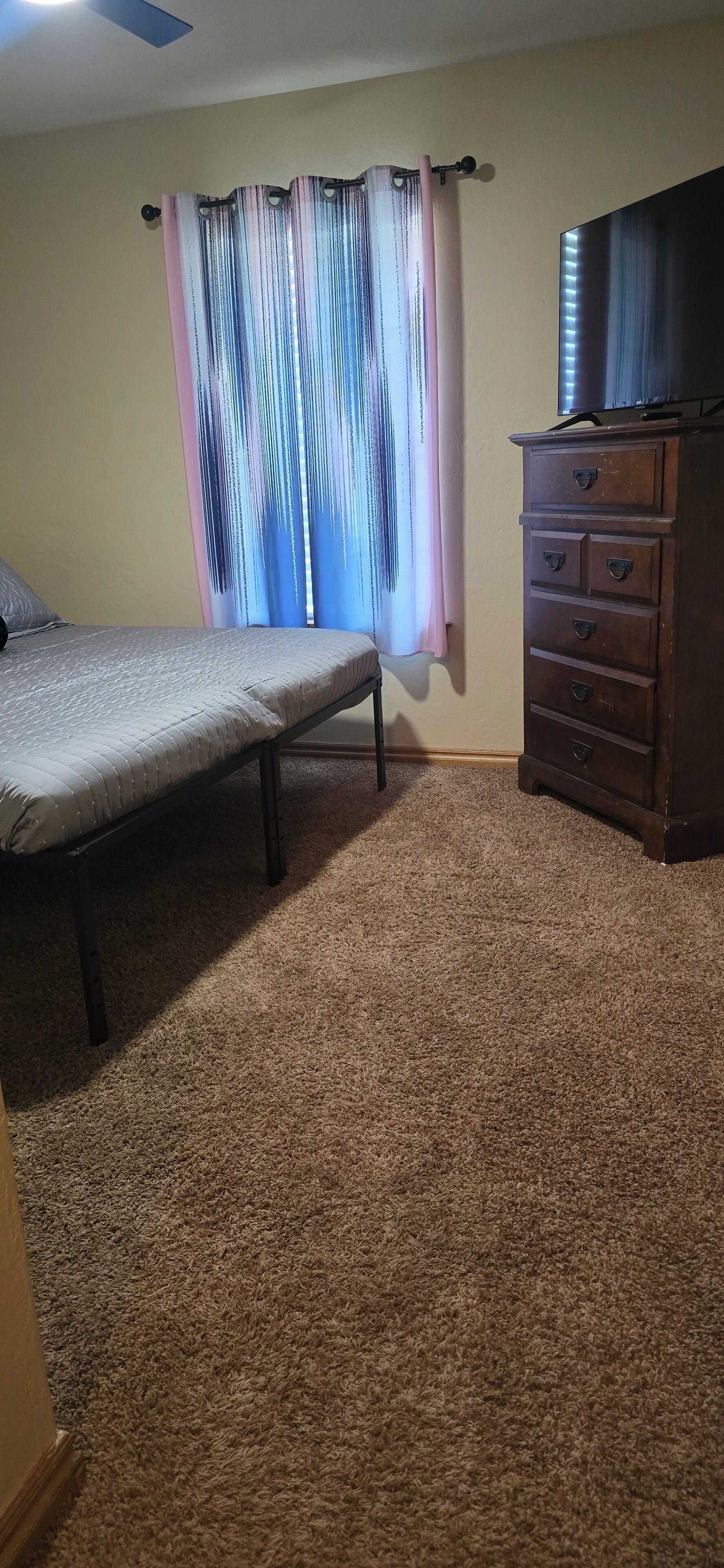 Une chambre à coucher avec un lit, une commode et une fenêtre avec des rideaux.