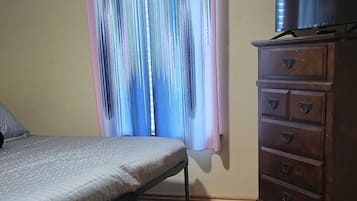 Ein Schlafzimmer mit einem Bett, einer Kommode und einem Fenster mit Vorhängen.