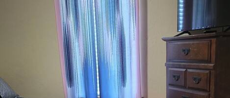 Une chambre à coucher avec un lit, une commode et une fenêtre avec des rideaux.