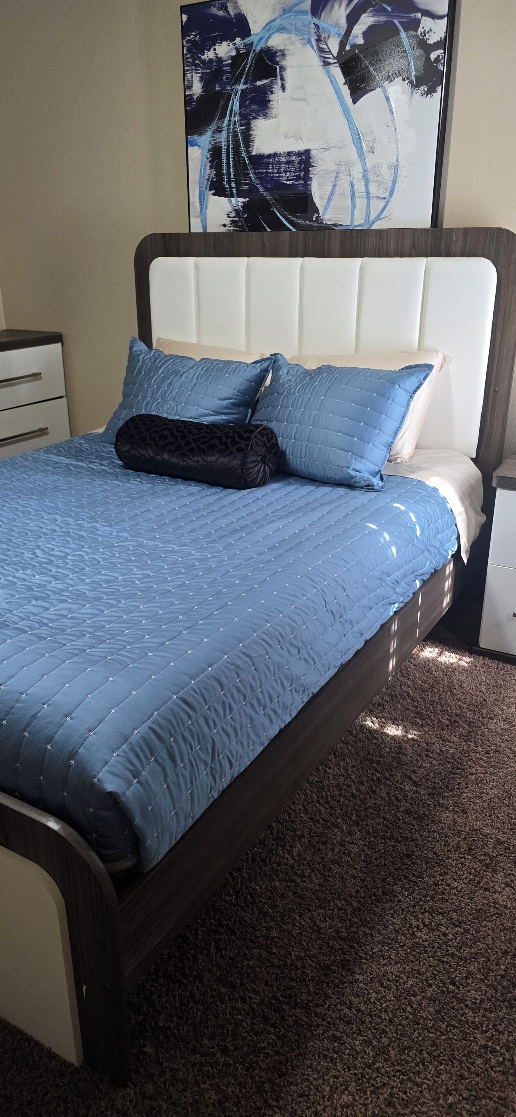 A bed with a quilted blue cover, a matching pillow, and a dark brown headboard.