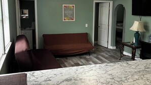 A room with a brown sofa, a marble table, a television, and a door leading to another room. - Downtown SRQ 3BR 2ba, Playground, Unit 1, Sleeps 6 (Sarasota)