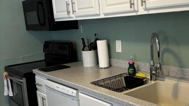 A kitchen with white cabinets, a black microwave, a dishwasher, a sink with a faucet, and a dish rack. - Downtown SRQ 3BR 2ba, Playground, Unit 1, Sleeps 6 (Sarasota)