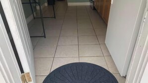 A hallway with a tiled floor leading to a door with a black mat. - Downtown SRQ 3BR 2ba, Playground, Unit 1, Sleeps 6 (Sarasota)