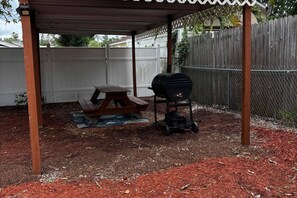 Ein überdachter Außenbereich mit Picknicktisch und Grill.