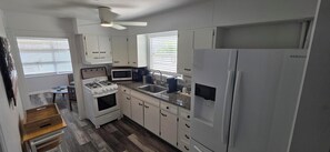 Une cuisine de taille réduite, avec des meubles blancs, une cuisinière, un four à micro-ondes et un réfrigérateur.