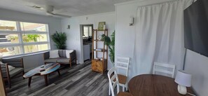 A modern living room with a sofa, a dining table, and a TV. - Most Photographed Bayfront-Amazing Sunset & Palm Trees on Exclusive Snug Harbor! (Stone Harbor)
