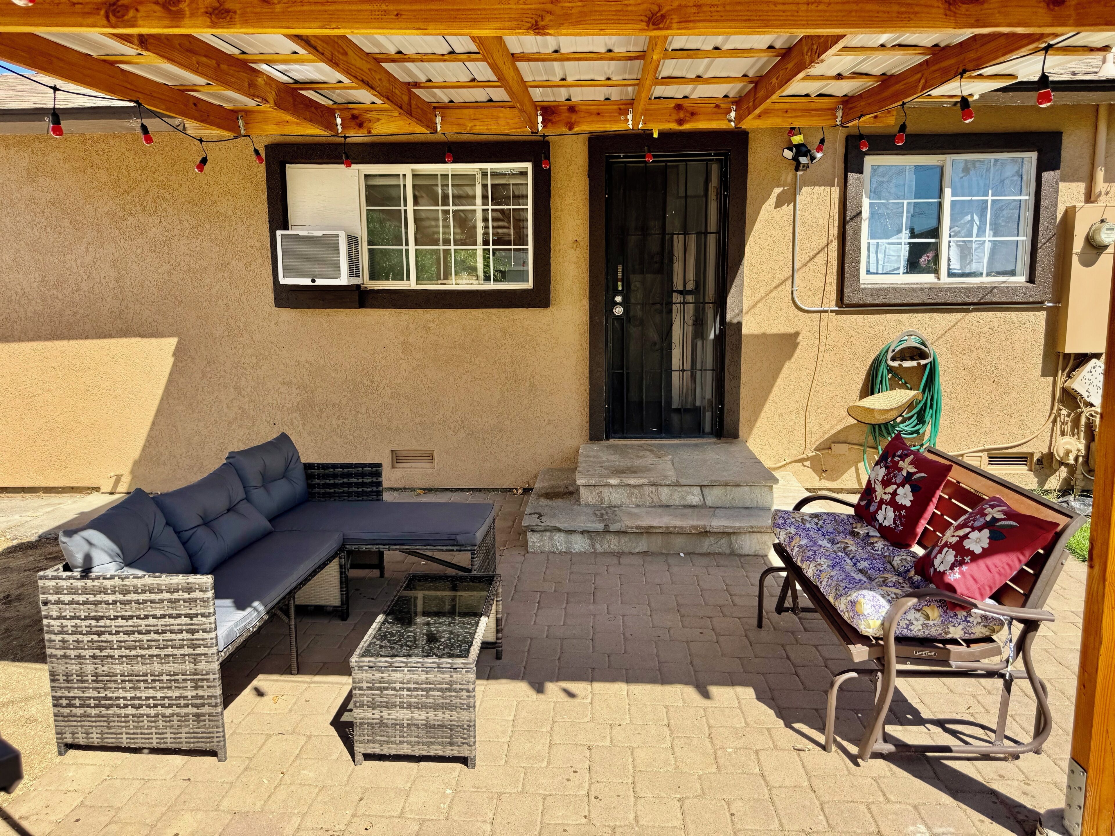 Un patio couvert aménagé avec du mobilier d’extérieur, notamment un canapé et un banc, et une porte surmontée d’une fenêtre.