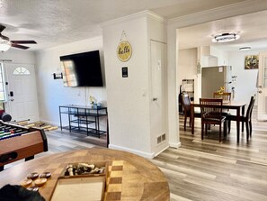 Una sala de estar con una mesa de fútbol de mesa, un televisor de pantalla plana y una zona de comedor con una mesa y sillas.