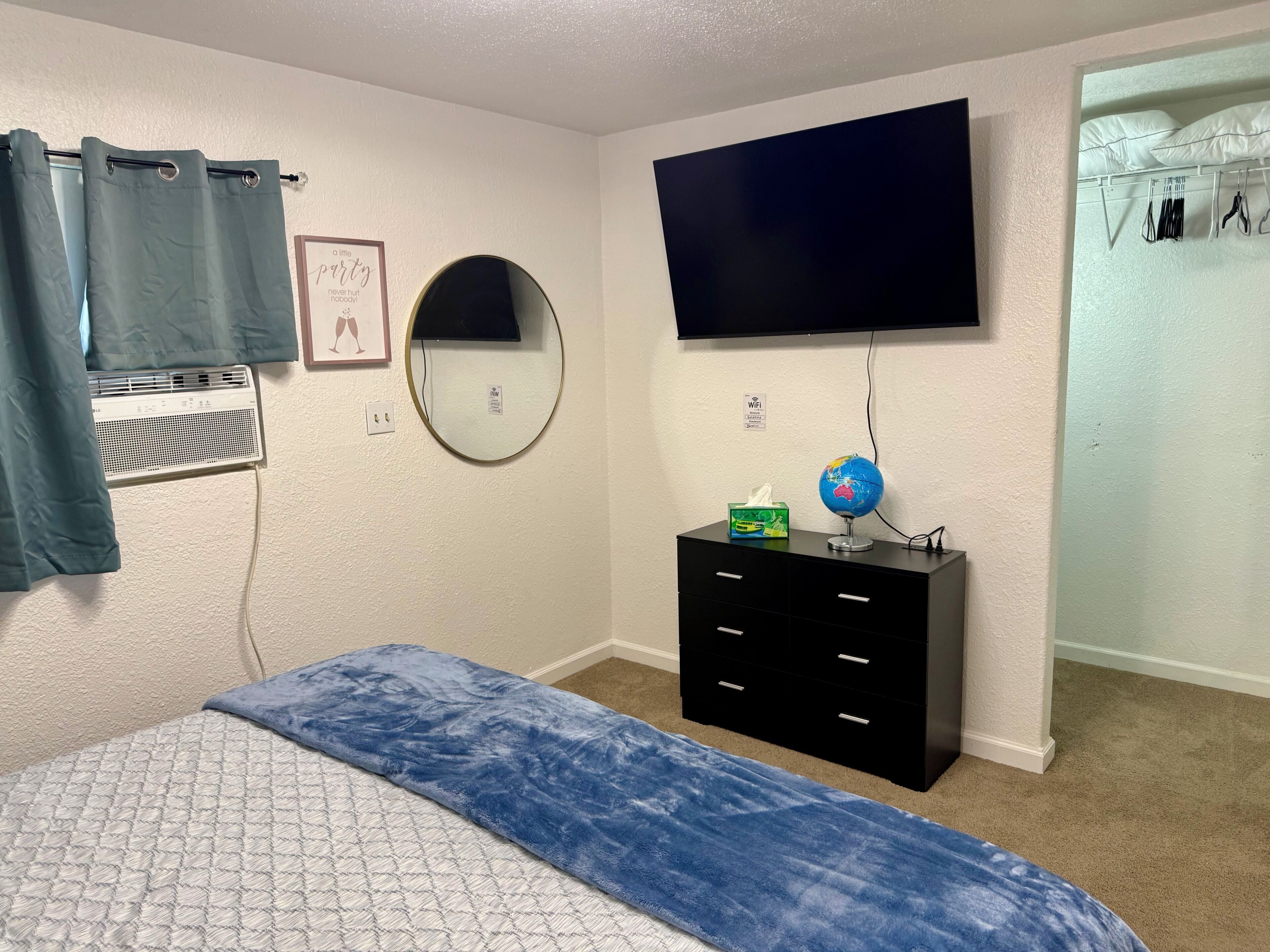 A bedroom with a bed, a dresser, a TV, a mirror, a globe, and a wall-mounted heater.