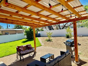 Un patio couvert agrémenté d’une pergola en bois, de meubles d’extérieur et d’un barbecue.