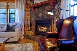 A cozy living room with a stone fireplace, leather armchair, and a sofa. - Rustic Cottage in Blue Ridge: Hot Tub • Mtn Views • Pets • Fire Pit • EV Charger (Mineral Bluff)
