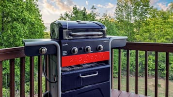 A gas grill with a digital display and control knobs, positioned on a wooden deck with a railing.