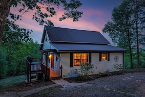 A two-story house with a porch, a deck, and a small garden area. - Rustic Cottage in Blue Ridge: Hot Tub • Mtn Views • Pets • Fire Pit • EV Charger (Mineral Bluff)