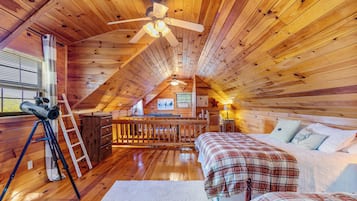 A cozy attic bedroom with wooden walls, a ceiling fan, a telescope, and a bed with plaid bedding.